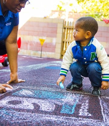 Child drawing Goodwill logo with sidewalk chalk with a goodwill volunteer