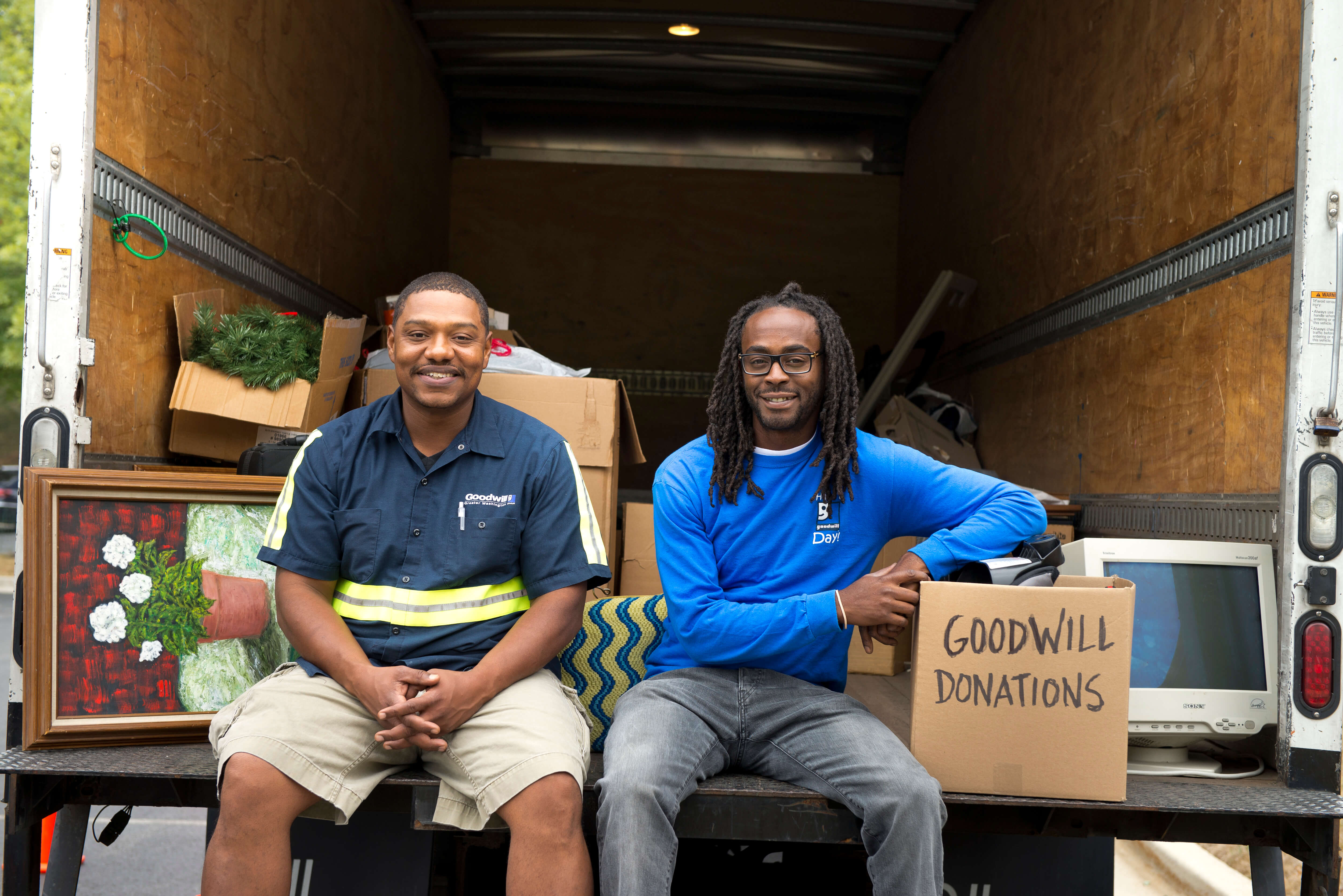 Two Goodwill drivers sitting in the back of the truck smiling with a box of donations