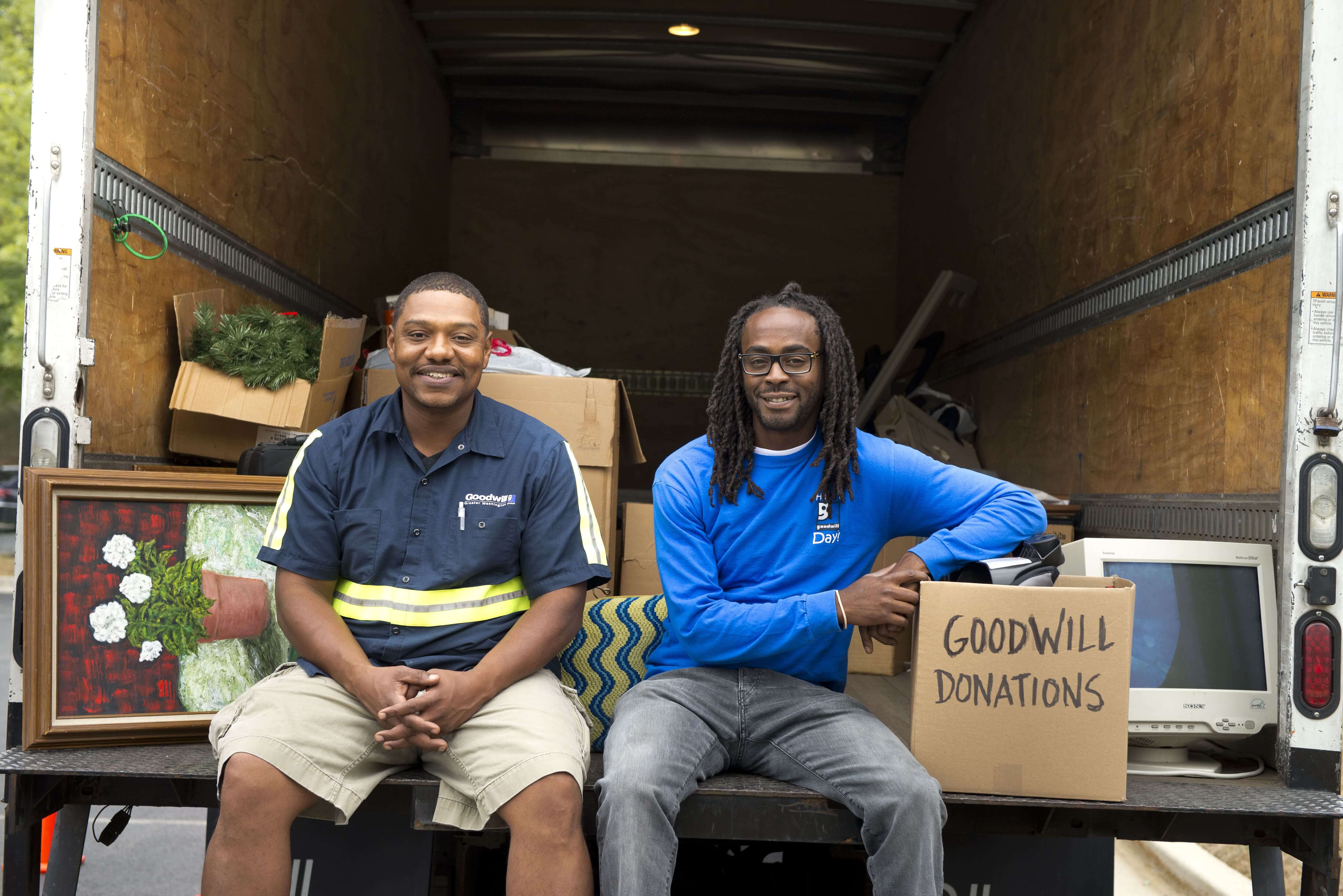 Two Goodwill drivers sitting in the back of the truck smiling with a box of donations