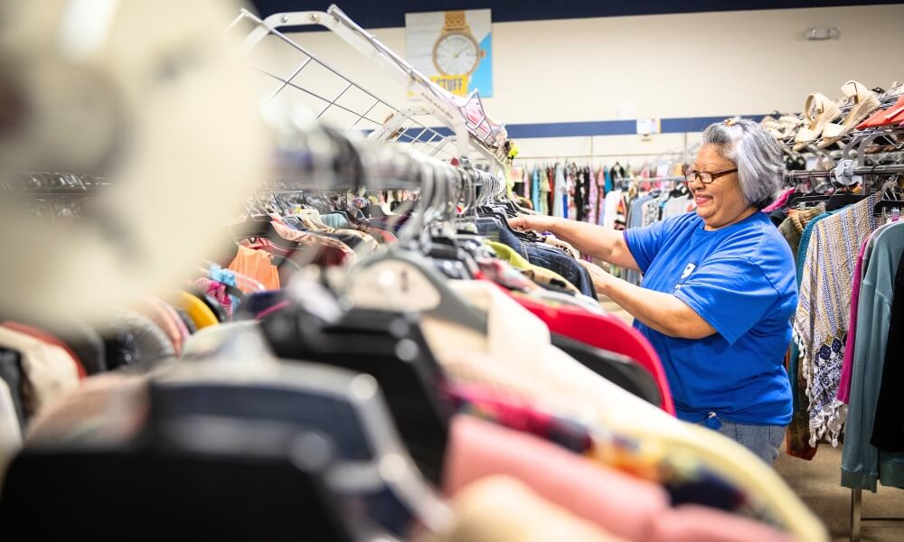 Goodwill employee hangs clothing on the rack on the sales floor